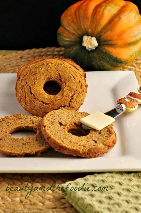 a plate containing Pumpkin Bagels and a butter knife with butter on it. A pumpkin sits in the background 