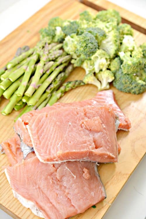raw salmon, asparagus, and broccoli on a bamboo cutting board 