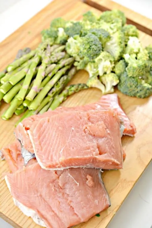 raw salmon, asparagus, and broccoli on a bamboo cutting board 