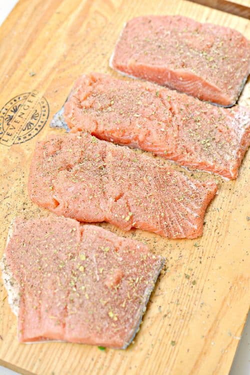 raw salmon sprinkled with garlic and herbs on a cutting board 