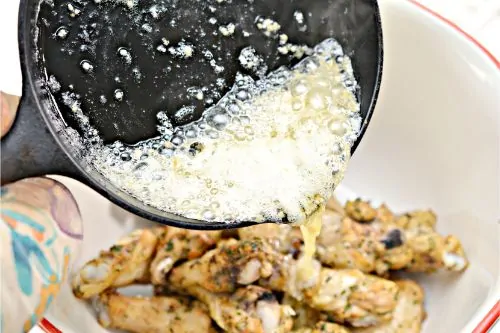 pouring butter mixture over cooked chicken wings