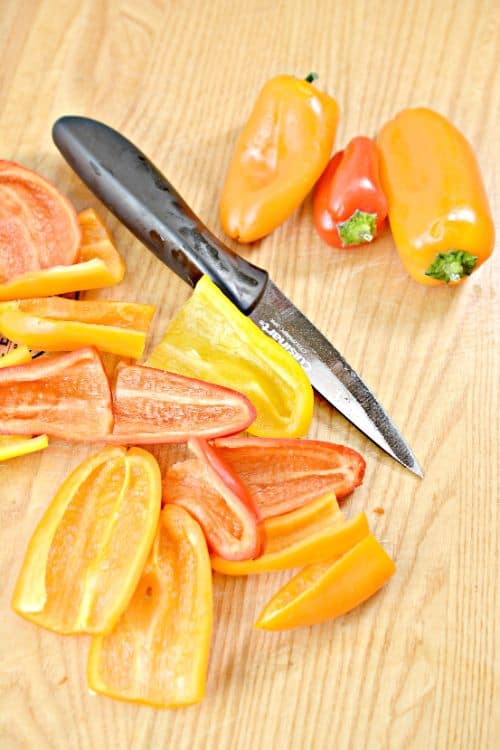 sliced red and yellow sweet mini peppers and a paring knife sitting on a bamboo cutting board 