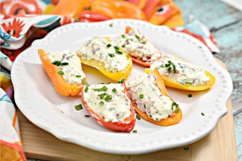 red and yellow cheese stuffed mini peppers arranged on a white plate sitting on a bamboo cutting board 