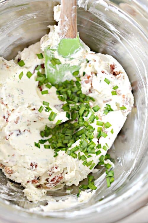 cream cheese, bacon, and chives in a stainless steel mixing bowl with a rubber spatula 