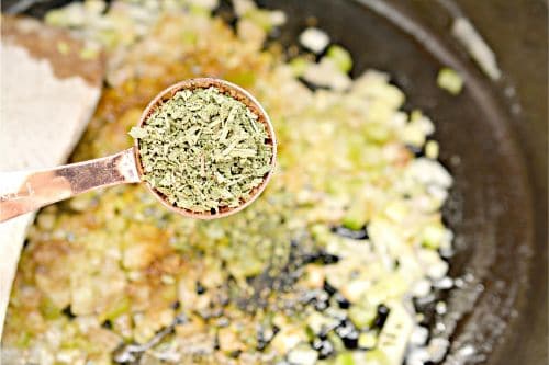herbs and spices in a tablespoon over a mixing bowl of stuffing 