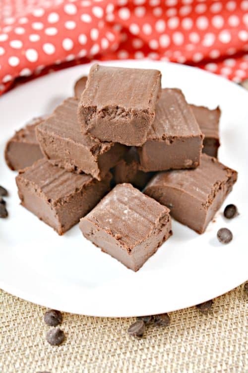keto chocolate peppermint fudge cut into squares and placed on a white plate with chocolate chips sprinkled around them 