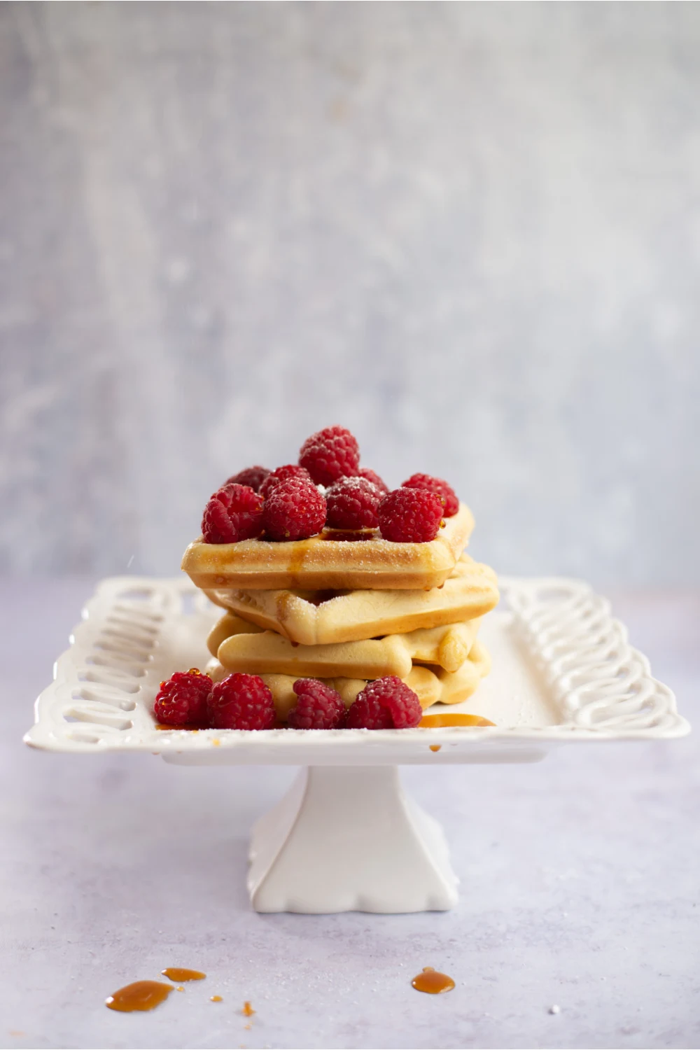 stack of low carb waffles covered in raspberries and syrup sitting on a white lacy plate