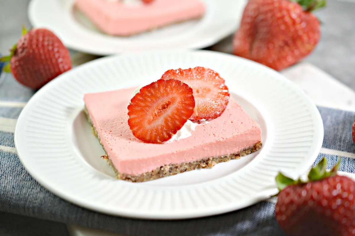 low carb strawberry cheesecake bar cut and sitting on a white plate topped with a sliced strawberry