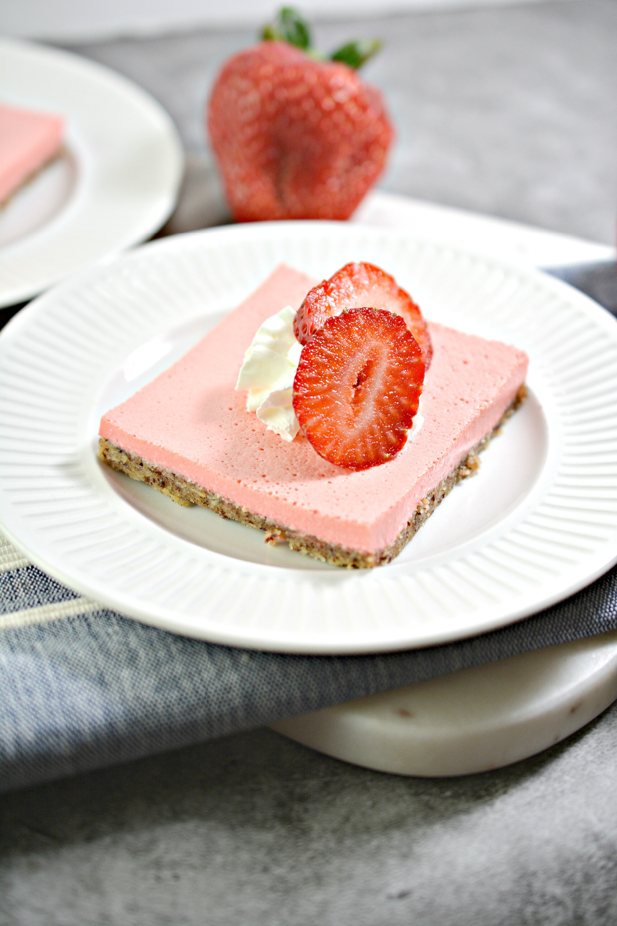 strawberry cheescake bar on a white plate with a strawberry in the background